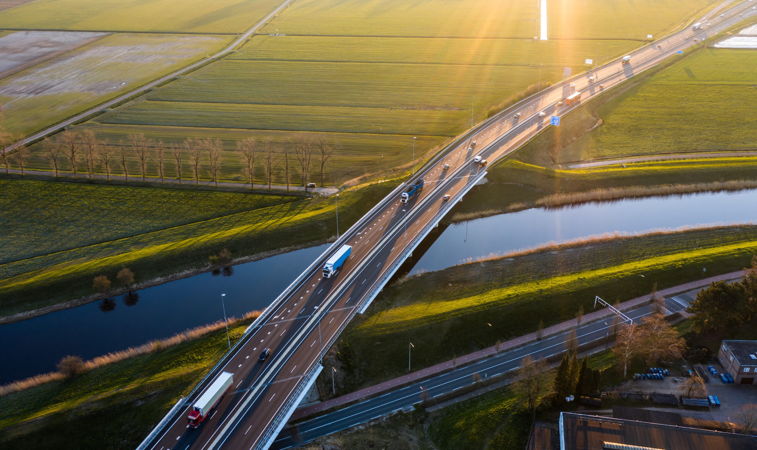 Väg med lastbilar över vatten i grönt soligt landskap