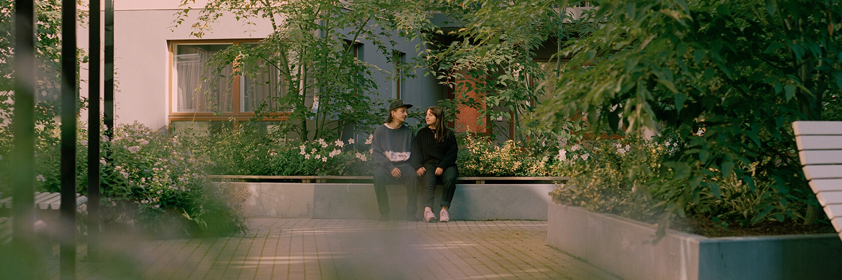 Man och kvinna sitter på bänk i grönskande bostadsområde