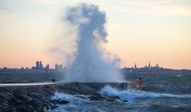 Stormiga vågor bryter mot pir med Tallinns stadslinje i bakgrunden