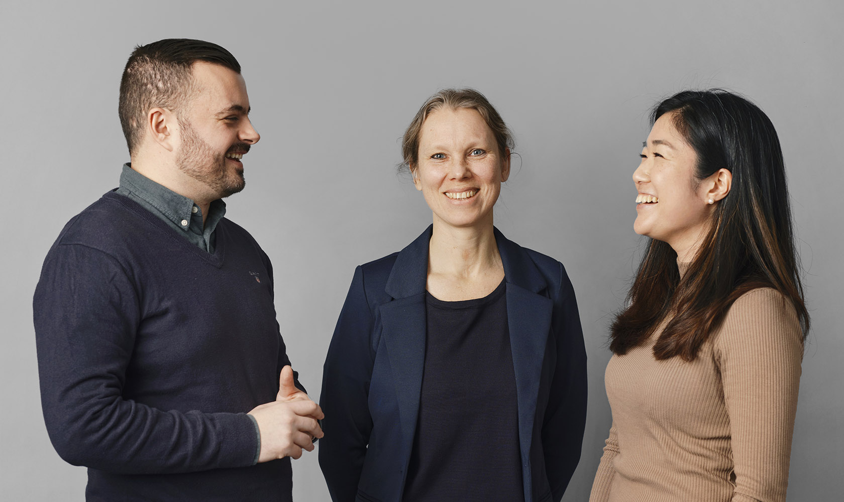 En man och två kvinnor pratar med varandra mot en grå bakgrund