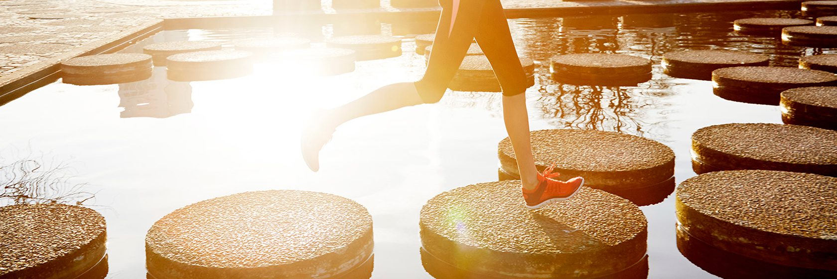 Joggande kvinna hoppande på stenar mellan vatten