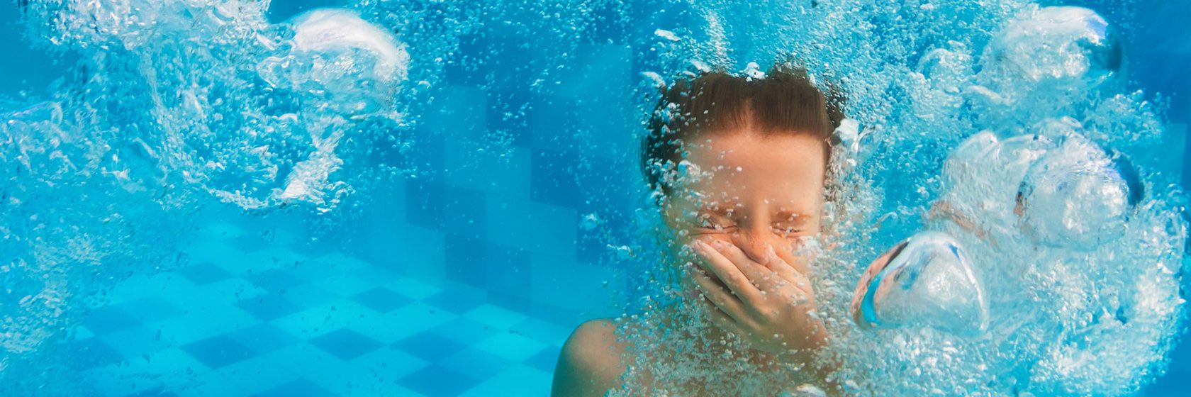 pojke håller för näsan under vattnet i bassäng