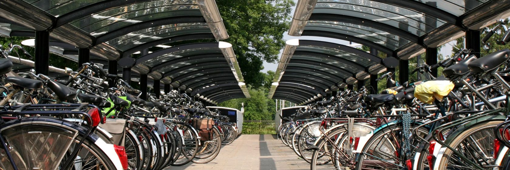 Två rader av cyklar i cykelställ under tak