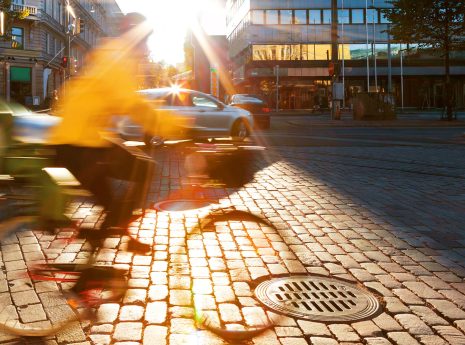 En cyklist i gul jacka cyklar på stenlagd gata