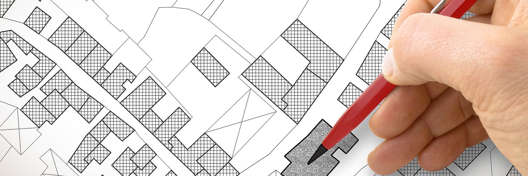 En hand håller i en penna och ritar ut fastigheter på en karta