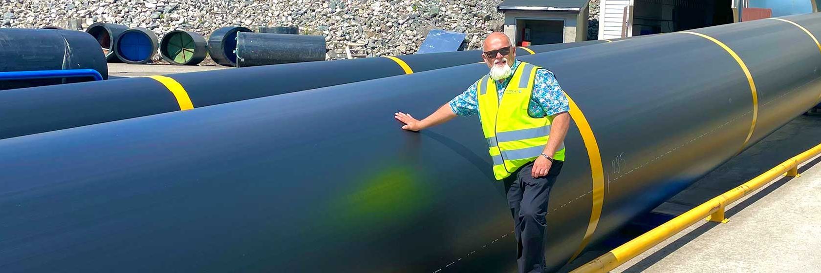 Man i vitt skägg står bredvid stora svarta vattenledningsrör