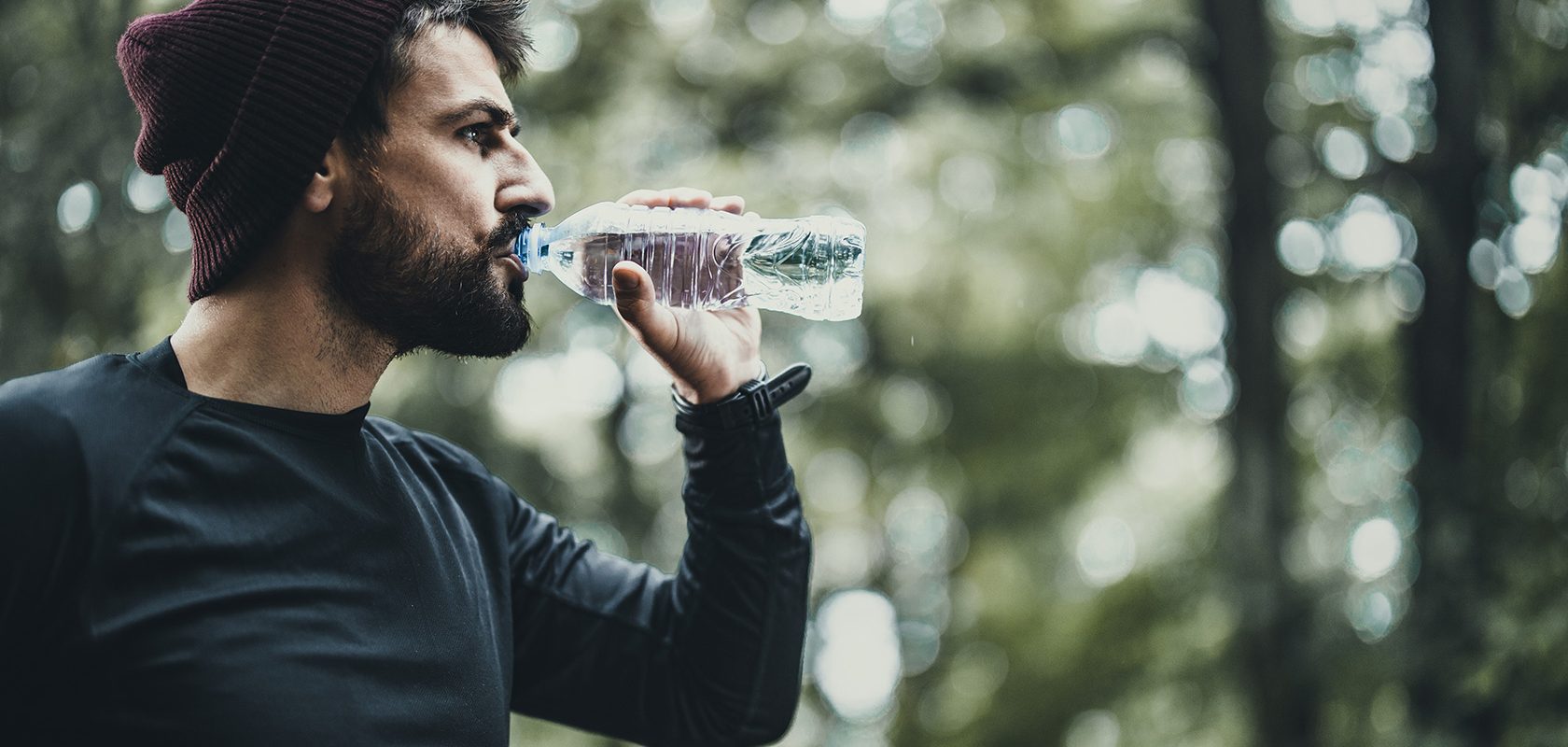 Man med mössa dricker vatten ur flaska