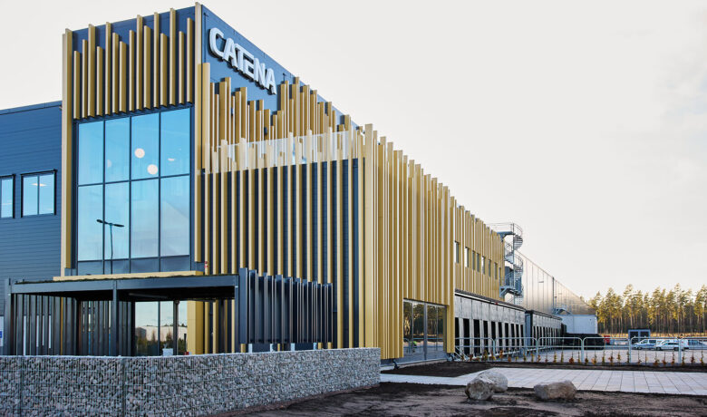 Träfasad av Catenas logistikbyggnad med Catenas logotyp på. Stenmur i förgrunden.