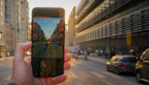 Beskuren hand som håller på mobil bakgrund mot stadsgatan
