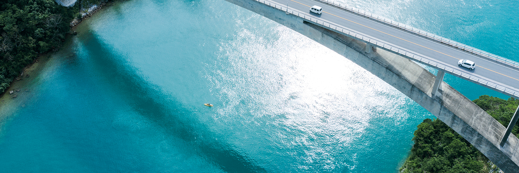 Betongbro över klarblått vatten med ett par bilar som passerar över bron
