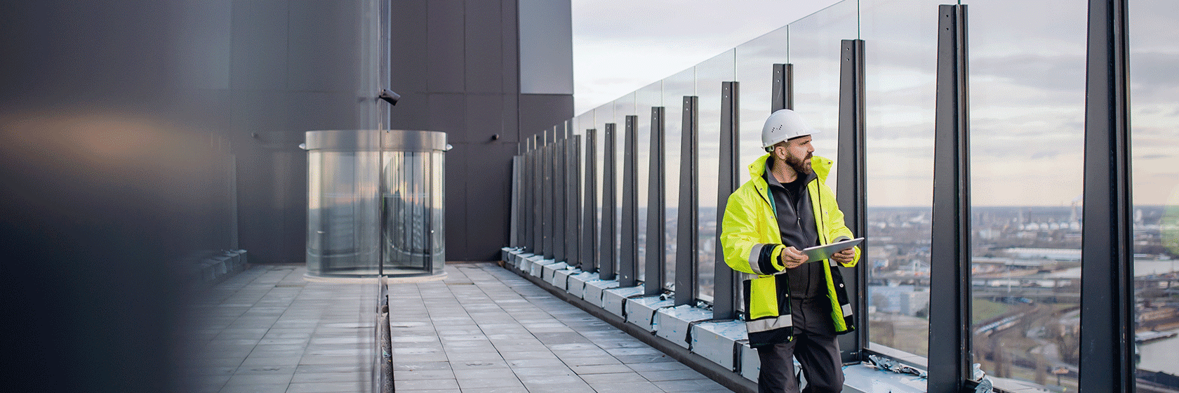 Man i varselkläder och bygghjälm inspekterar något på en kontorsfastighets terass