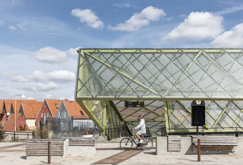 Man cyklar förbi modern glasstruktur med röda tak på byggnader i bakgrunden.