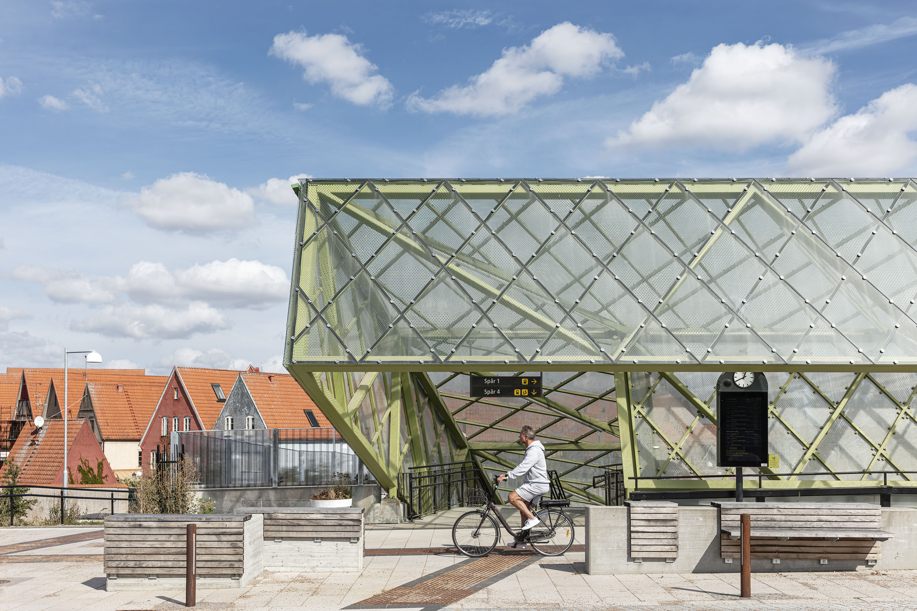 Man cyklar förbi modern glasstruktur med röda tak på byggnader i bakgrunden.