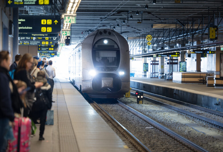 Tåg ankommer Stockholms C i motljus. Människor väntar på perrongen.