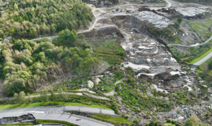 Flugfoto över område där stora vattenmassor orsakas skred. Träd, lera och en väg som har skadats.
