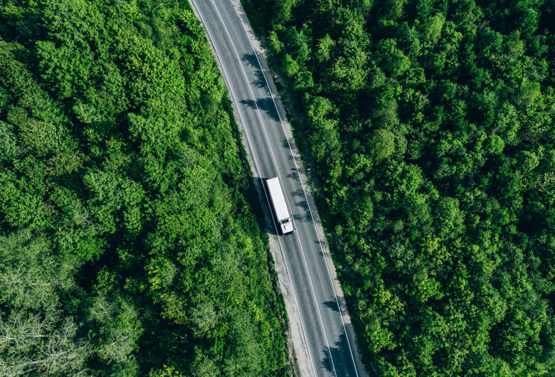 En lastbil kör på en väg kantad av grön skog på båda sidor av vägen