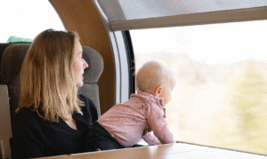 Ung mamma med spädbarn i rosa kläder som tittar ut genom tågfönstret