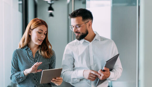 Kollegor diskuterar arbete i en modern kontorsmiljö, håller tablets och laptop.