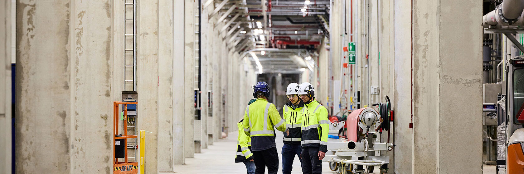 Fyra arbetare i skyddsutrustning står och pratar i en industrihall.