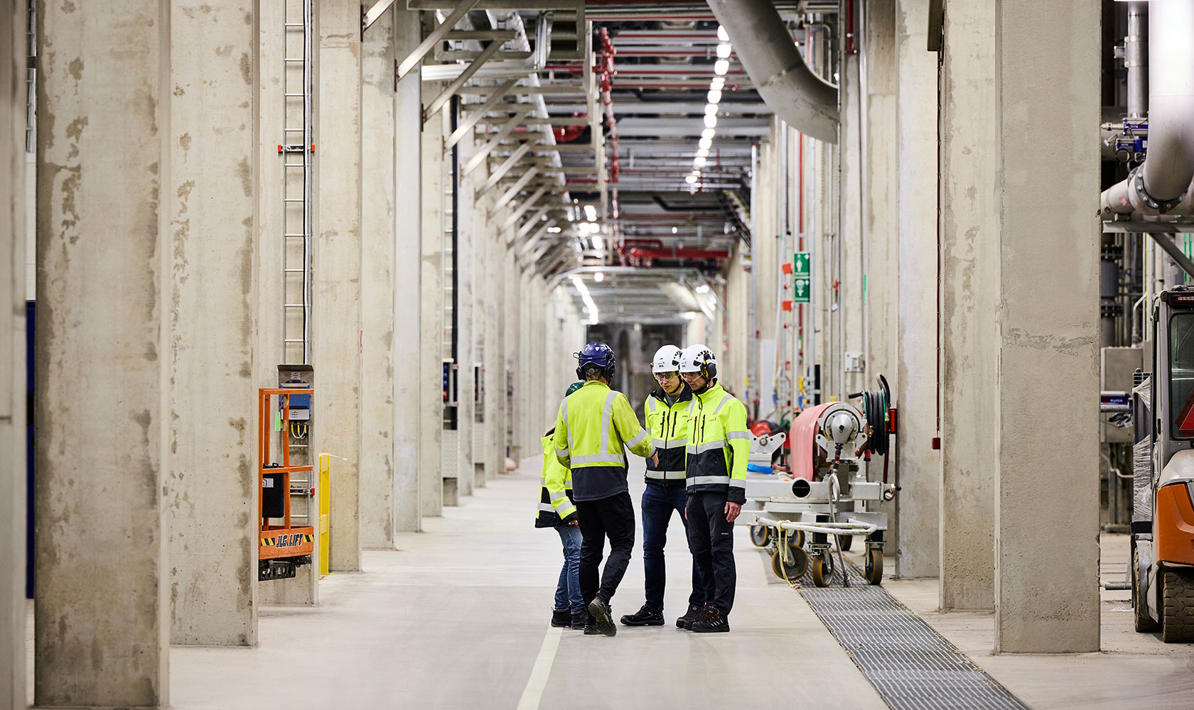 Fyra arbetare i skyddsutrustning står och pratar i en industrihall.