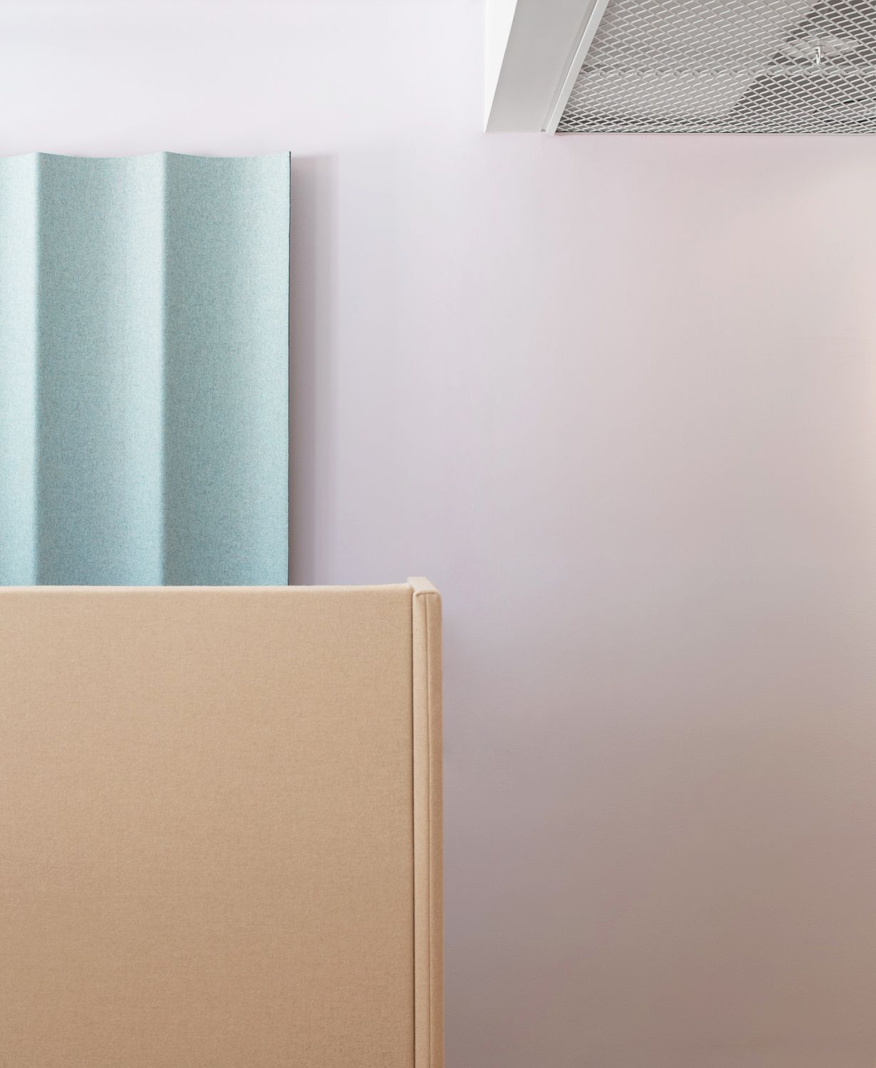 Beige rumsavdelare framför ljusrosa vägg med mintgrönt vikbart akustikpanel och vit takgaller.