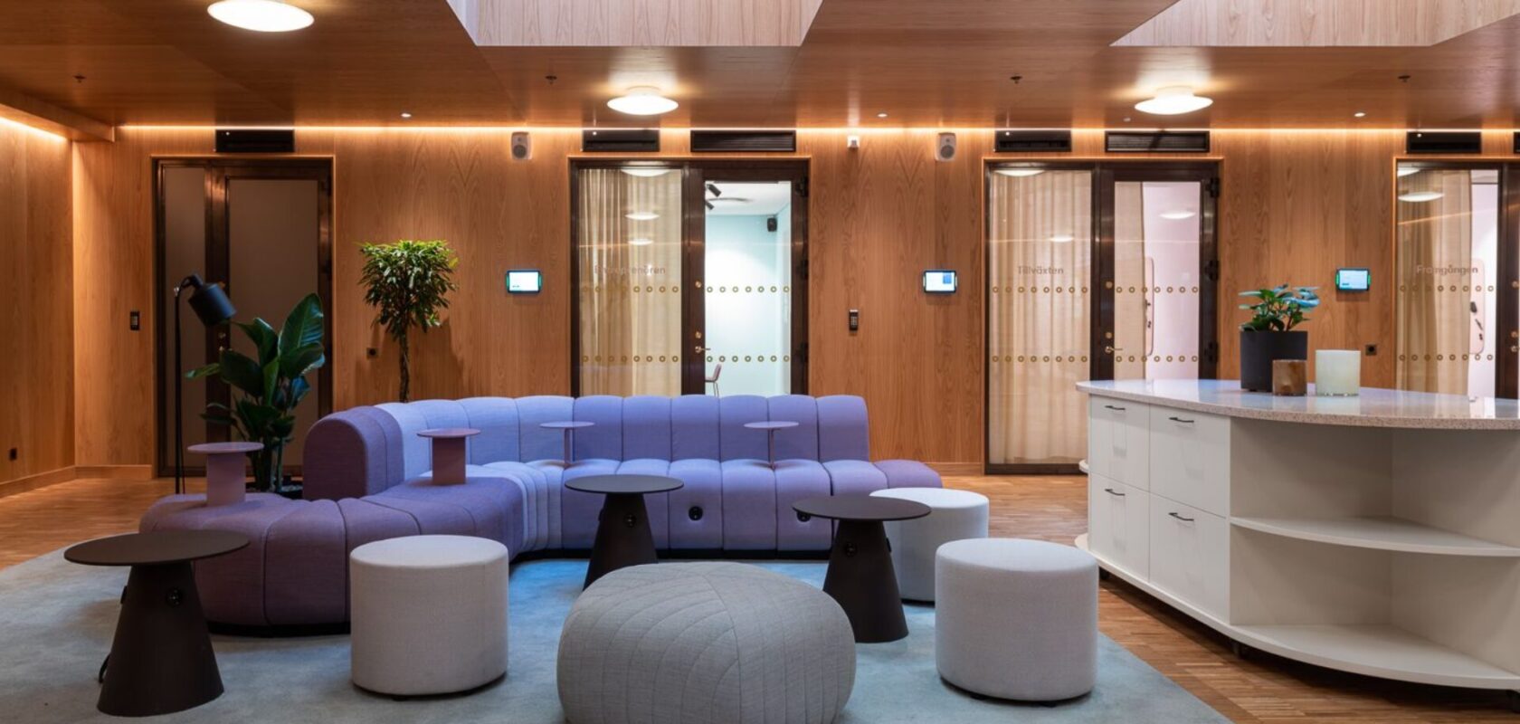 Modern kontorslounge med lila soffor, träpaneler och elegant inredning.