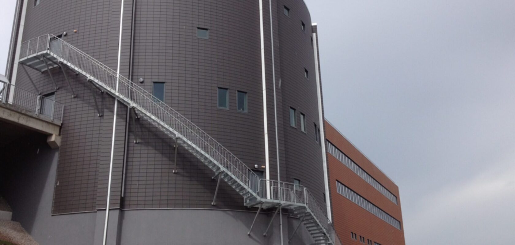 Modern byggnad med metalltrappor på utsidan, grå fasad och rektangulära fönster.