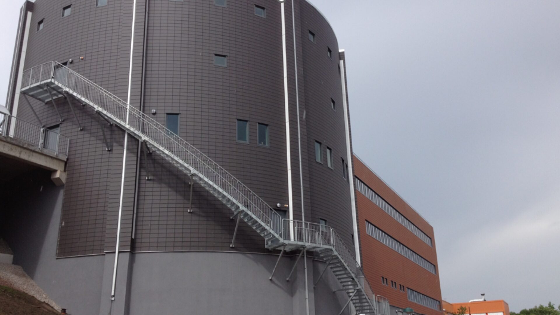 Modern byggnad med metalltrappor på utsidan, grå fasad och rektangulära fönster.