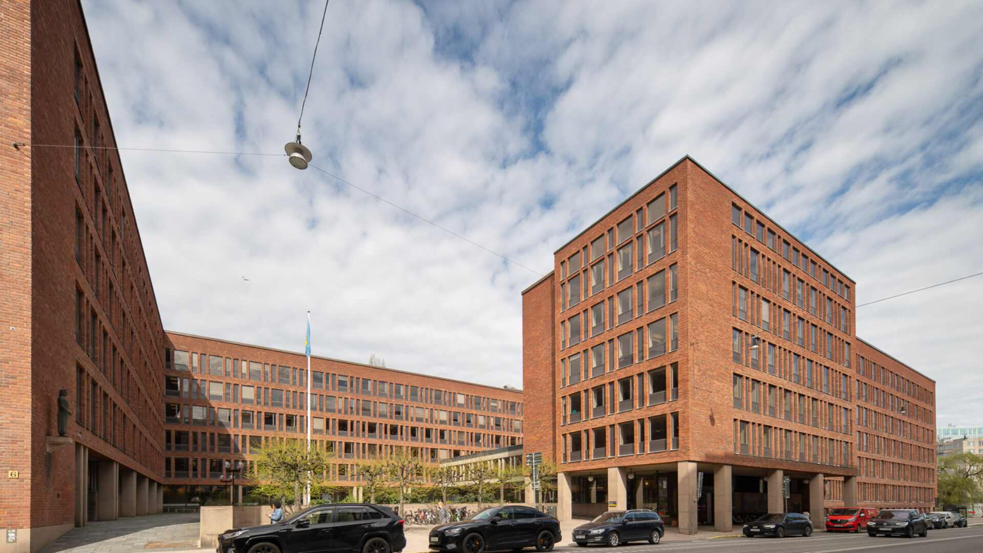 Kontorsbyggnader i rött tegel runt en öppen gård, parkerade bilar och svensk flagga.