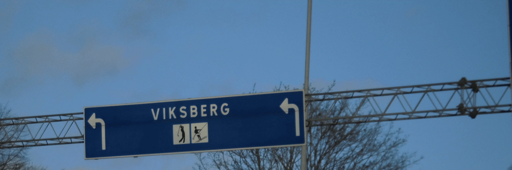 Vägskylt med ortsnamn mot gråblå himmel
