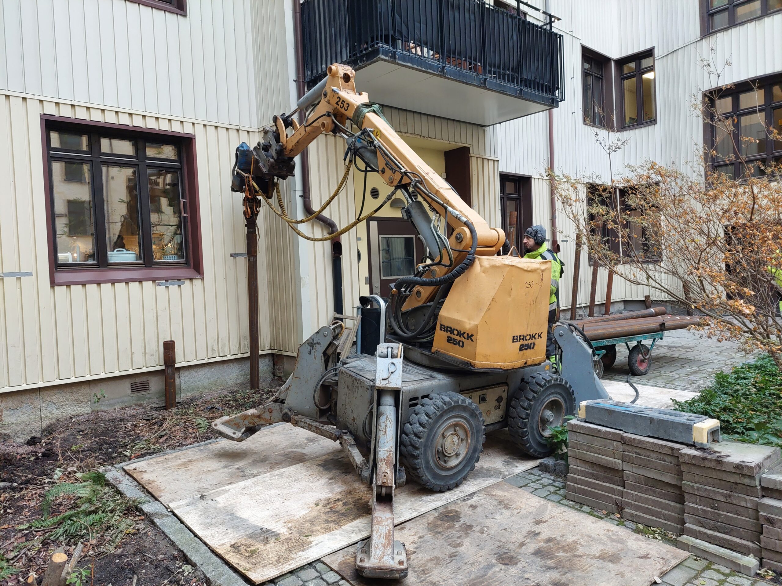 Gul byggnadsrobot Brokk 250 som arbetar vid lägenhetskomplex med beige fasad och mörka fönster.