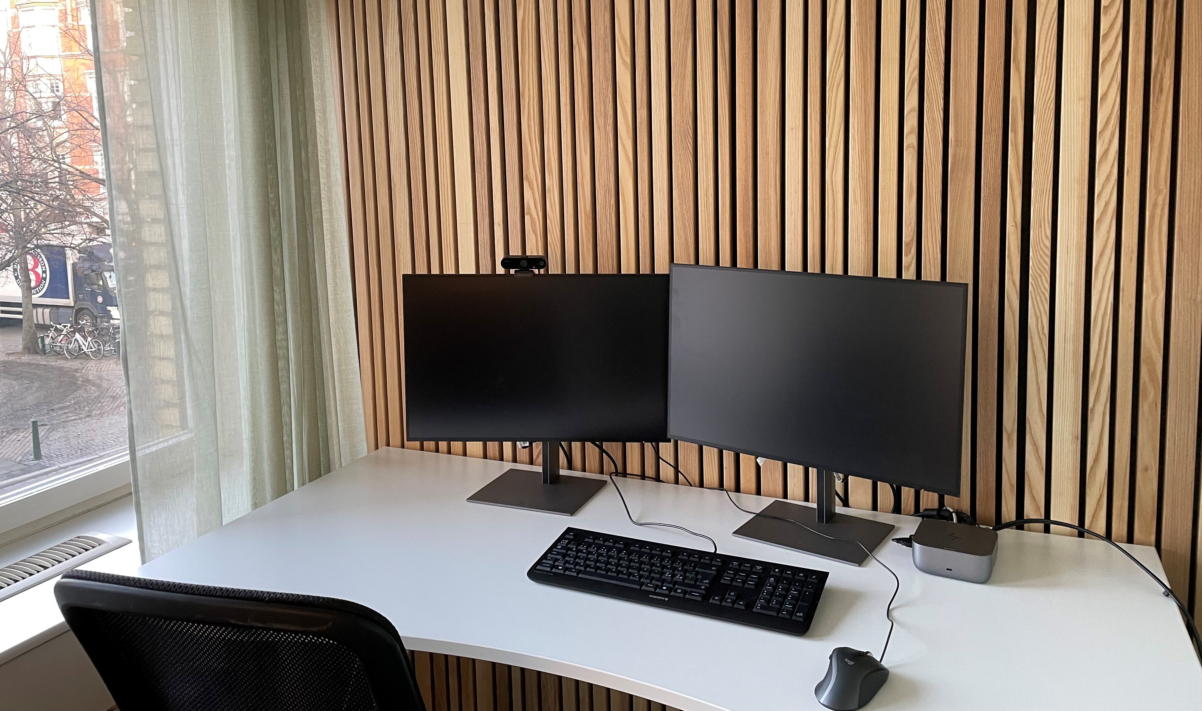 Skrivbord med två bildskärmar och tangentbord mot vägg med träpanel