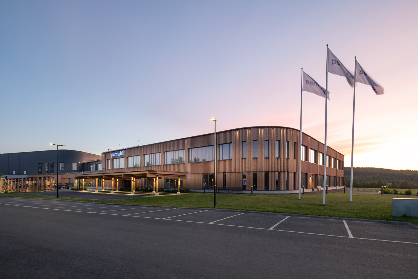 Kontrosbyggnad i trä med flaggor och parkering i förgrunden