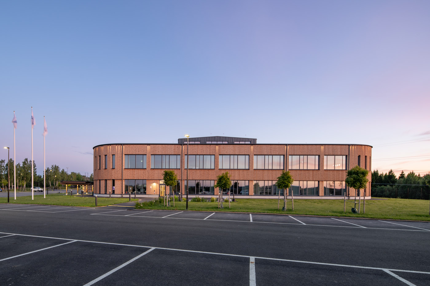 Kontorsbyggnad i trä med parkering i förgrunden.