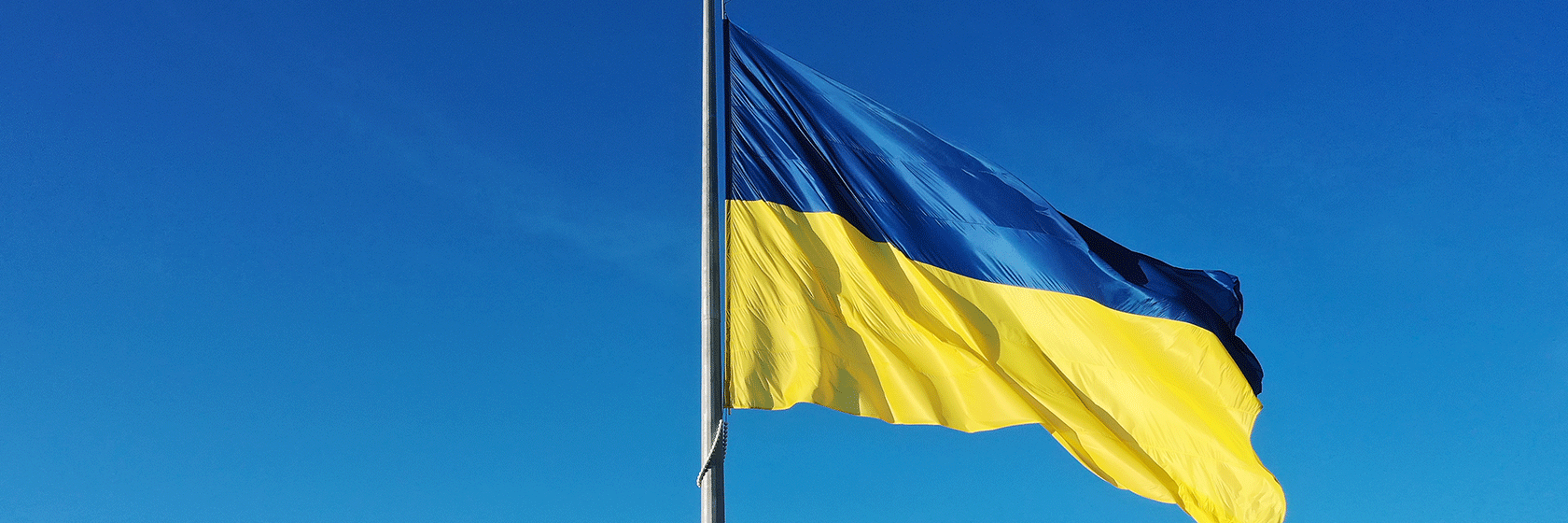 Ukrianas blågula flagga vajar i vinden med en klarblå himmel i bakgrunden