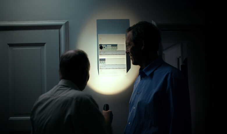 Två personer kontrollerar elcentral i mörkt rum med ficklampa