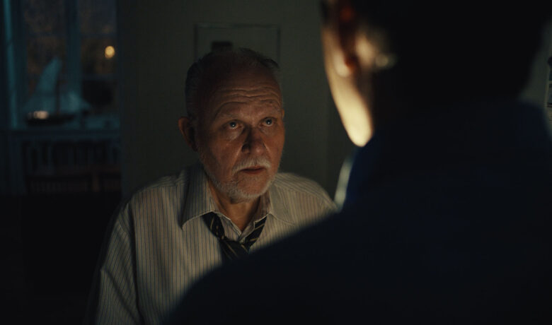 Äldre man med står i mörkt rum mitt emot yngre person