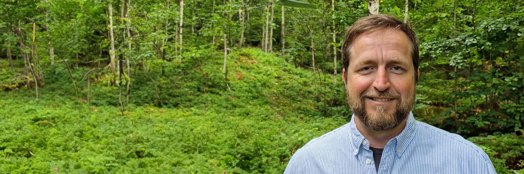 David Hirdman i ljusblå skjorta med grön skogsmark i bakgrunden