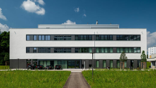 Modern kontorsbyggnad med vit fasad, stora fönster och parkeringsplats framför.