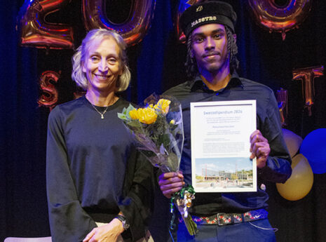 Två personer på prisutdelning med blommor och diplom, festballonger i bakgrunden