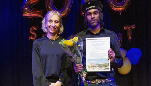 Två personer på prisutdelning med blommor och diplom, festballonger i bakgrunden
