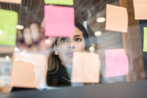 Kvinna syns bakom glasvägg fylld med olikfärgade postit-lappar