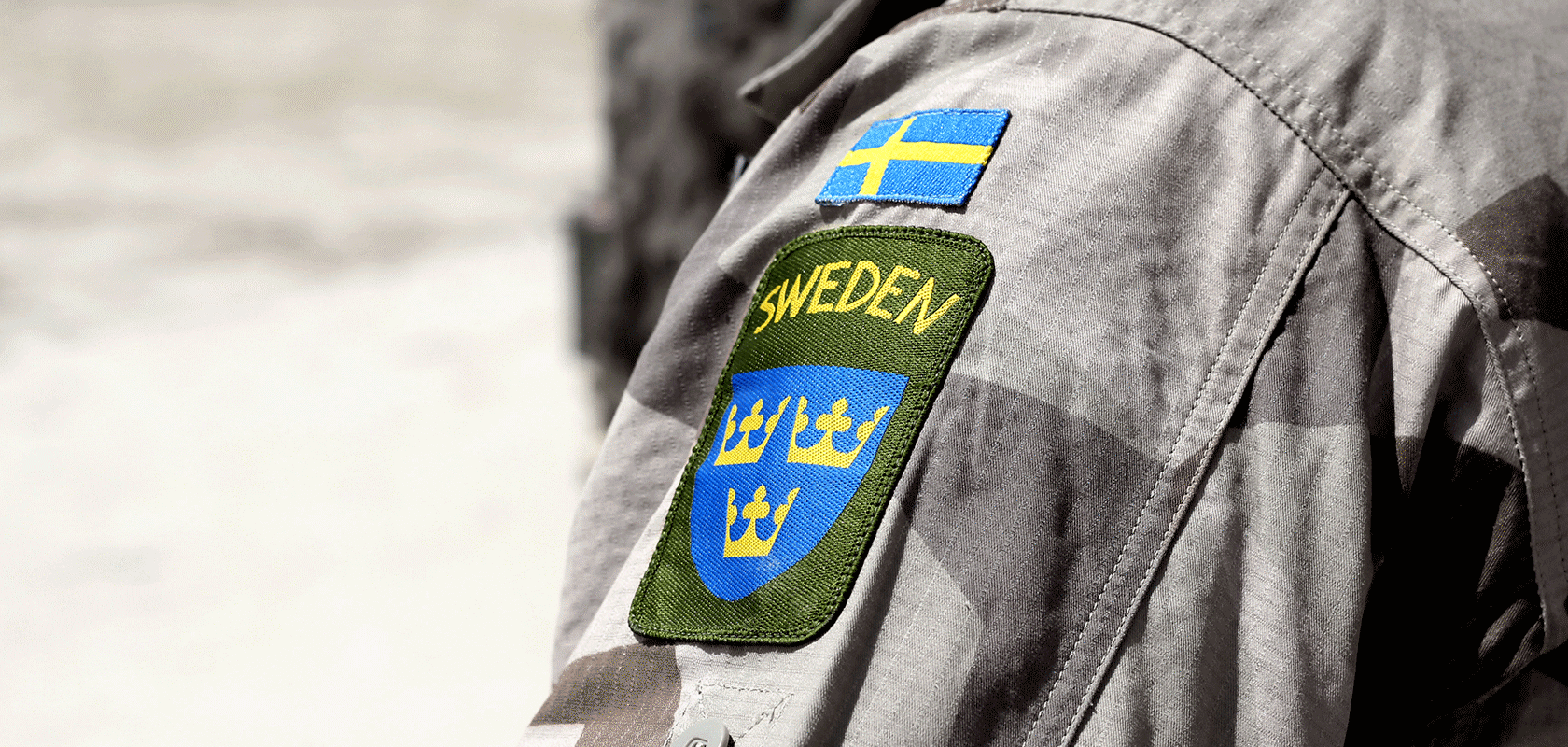 Armen på en person med militärjacka och svensk flagga samt Sweden och tre kronor broderat på ärmen