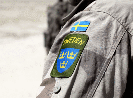 Armen på en person med militärjacka och svensk flagga samt Sweden och tre kronor broderat på ärmen