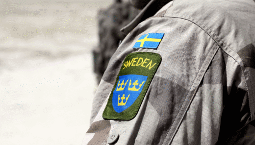 Armen på en person med militärjacka och svensk flagga samt Sweden och tre kronor broderat på ärmen