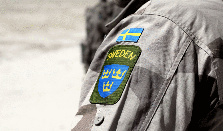 Armen på en person med militärjacka och svensk flagga samt Sweden och tre kronor broderat på ärmen