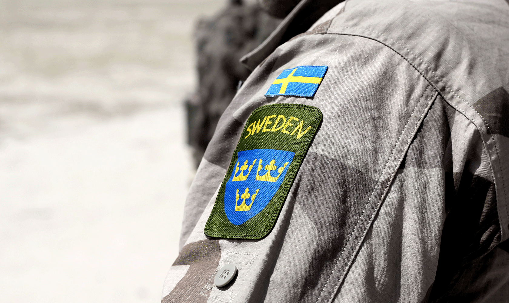 Armen på en person med militärjacka och svensk flagga samt Sweden och tre kronor broderat på ärmen