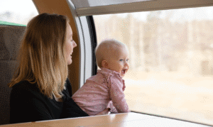 Kvinna i svart tröja håller 1-årigt barn i rosa tröja. Barnet tittar ut genom tågfönstret.
