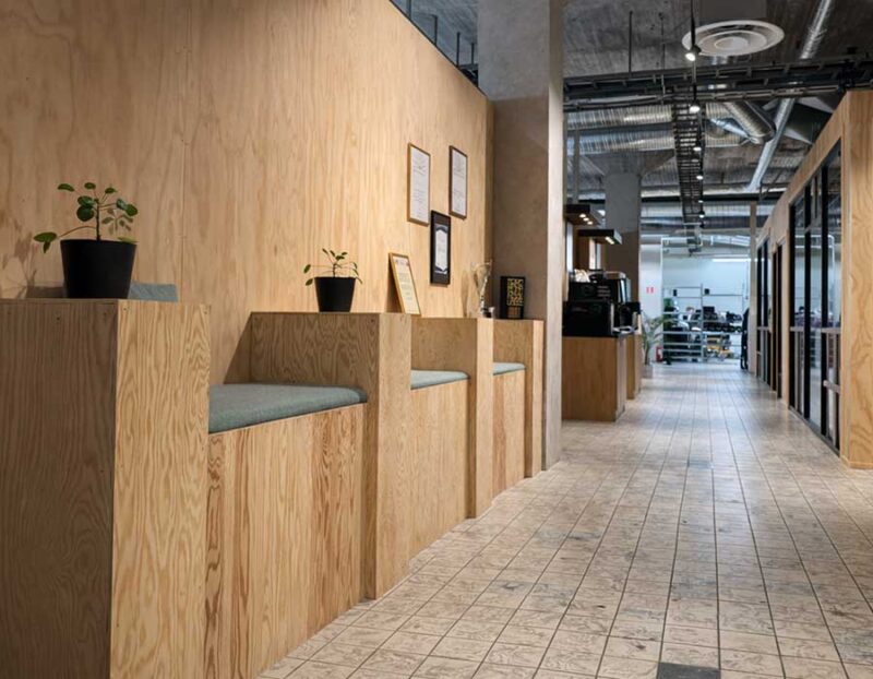 Modern kontorskorridor med träpanel, sittbänkar och glasade mötesrum i coworkingmiljö